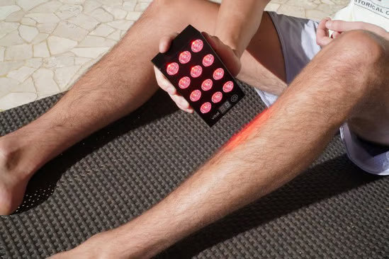 A man using the Vital Charge red light therapy device on his legs and feet